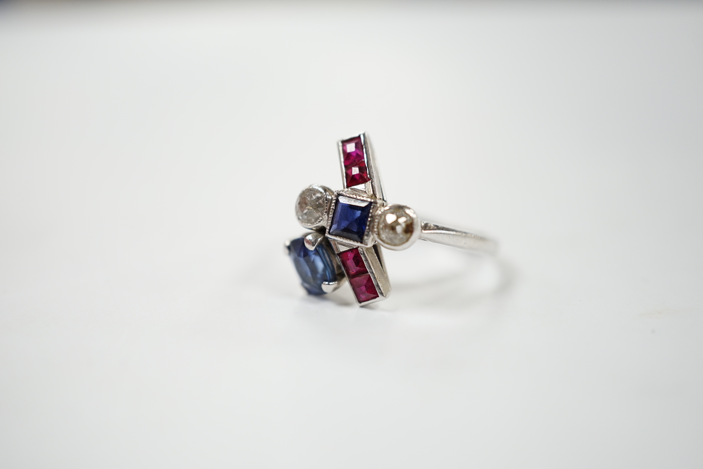 An unusual 1920's/1930's platinum, ruby, sapphire and diamond cluster set dress ring, of free form, the stones in a millegrain, claw or collet settings, size I, gross weight 3.7 grams.